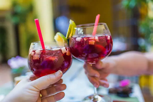 A couple celebrating while clicking two glasses of refreshing sangria with different fruits.