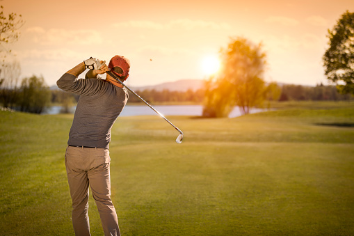Male golf player swinging club at beautiful sunset in background, with empty copyspace.