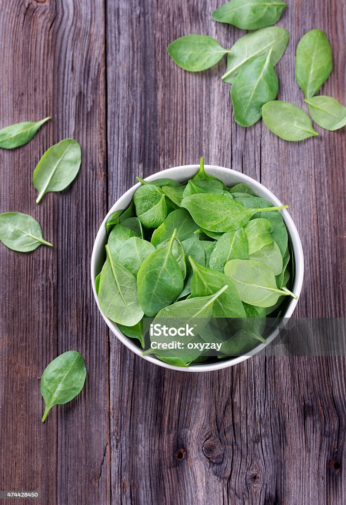 Fresh spinach in bowl Fresh spring baby leaves of spinach with water drops in bowl, on a old grungy table 2015 Stock Photo