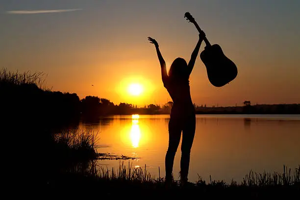 Photo of silhouette of a happy girl with a guitar by the river