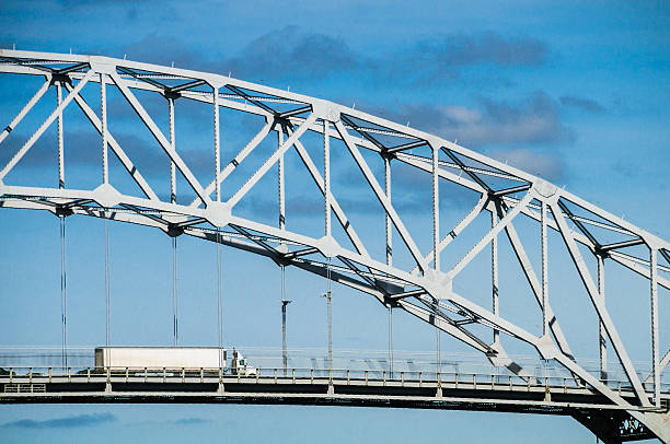 A white semi trailer truck with unmarked sides heads north over the Sagamore Bridge crossing the Cape Cod Canal in Bourne, Massachusetts.  This aging bridge, built in 1935, is one of two that connect Cape Cod to the Massachusetts mainland.