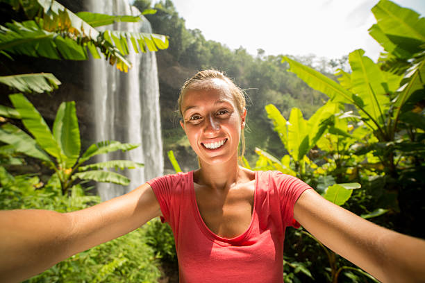 istock Young woman in rain forest  takes selfie with waterfall 474448086