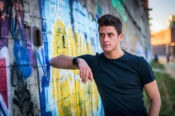 istock Attractive young man standing against colorful graffiti wall 474458202