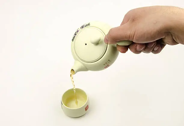 Horizontal photo, of the clay teapot tea flow in cup on white background, isolated, tea ceremony.