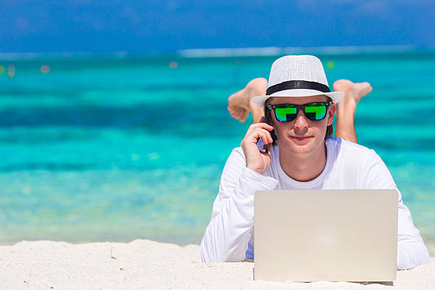istock Young man with laptop and cell phone on tropical beach 474460926