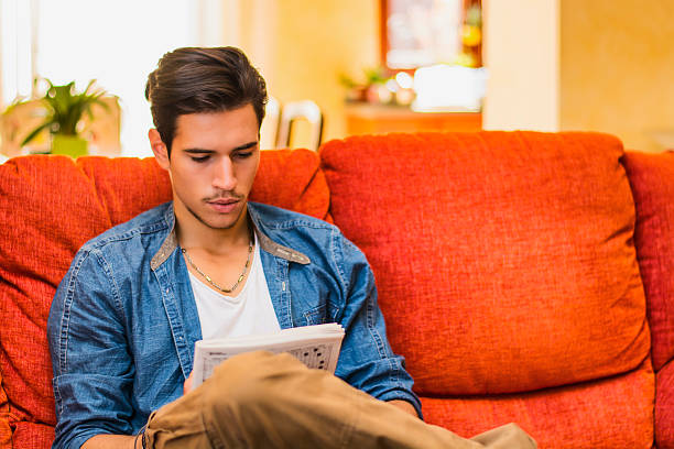istock Young man doing a crossword puzzle looking thoughtfully at magazine 474467696