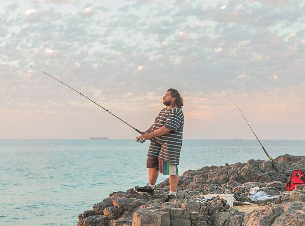 Senior fisherman casting out his fishing line into the sea from the rocky shoreline.