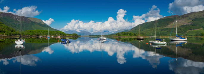 White fluffy clouds, green hills, blue sky and moored yachts reflecting in the perfectly still waters of Loch Leven at Glen Coe deep in the Highlands of Scotland, UK. ProPhoto RGB profile for maximum color fidelity and gamut.