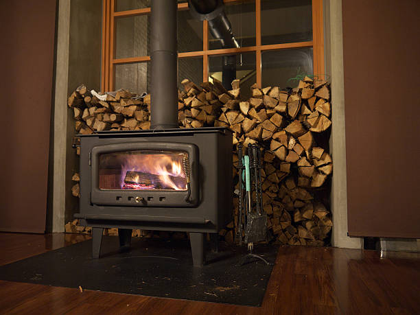 Wood burning stove Burning wood stove with pile of firewood in bundles next to the window wood burning stove stock pictures, royalty-free photos & images