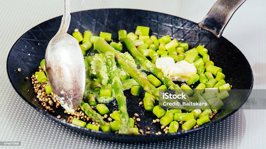 Cooking asparagus Pearl barley, asparagus and hemp seeds are fried in a pan and stir with a spoon. 2015 Stock Photo