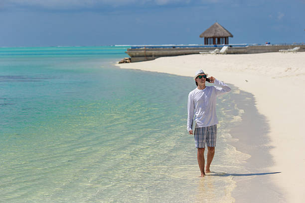istock Young man talking by cell phone on tropical beach 474471302