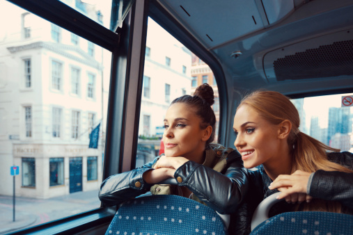 Two happy young women sitting on the bus and looking through window.