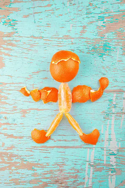 Human Figure Made of Fresh Orange Tropical Fruit Slices and Peel on Rustic Grunge Blue Wood Background, Top View
