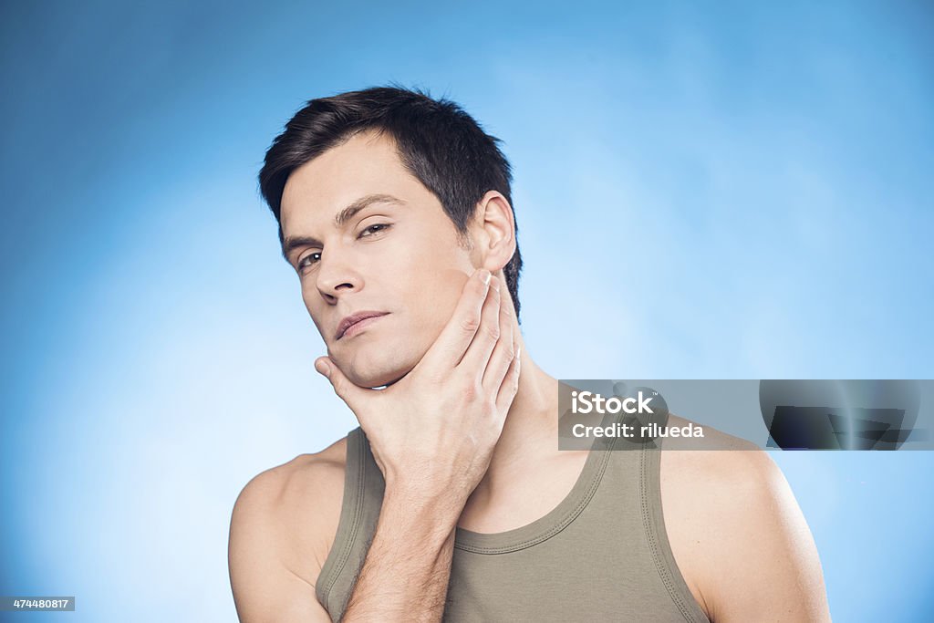Handsome man touching his face Handsome man in tank top touching his face as if to check if he's well shaved Adult Stock Photo