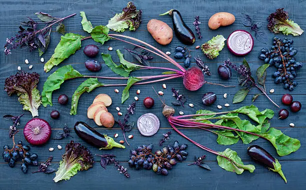 Collection of fresh purple fruit and vegetables on the black wooden table