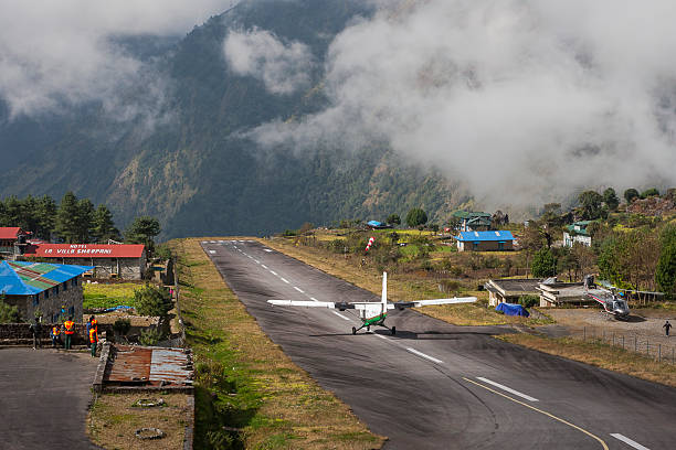 plane on the runway at Lukla airport Lukla, Nepal - October 28, 2013: Tenzing-Hillary Airport  also known as Lukla Airport, is a small airport in the town of Lukla, in Khumbu, Solukhumbu district, Sagarmatha zone, eastern Nepal. A program titled Most Extreme Airports, broadcast on The History Channel in 2010, rated the airport as the most dangerous airport in the world. In January 2008 the airport was renamed in honor of Sir Edmund Hillary and Sherpa Tenzing Norgay, the first people to reach the summit of Mount Everest and also to mark their efforts in the construction of this airport. The airport is popular because Lukla is the place where most people start the climb to Mount Everest Base Camp. There are daily flights between Lukla and Kathmandu during daylight hours in good weather. Although the flying distance is short, rain commonly occurs in Lukla while the sun is shining brightly in Kathmandu.  airport porter stock pictures, royalty-free photos & images