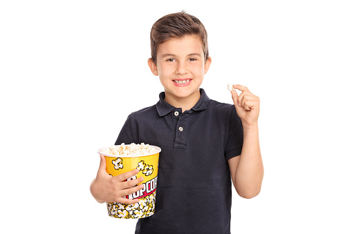 Joyful kid holding a big box of popcorn and looking at the camera isolated on white background