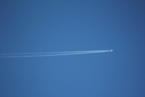 An Aircraft with a white vapor trail in the clear blue sky. It is a beautiful day without any clouds.