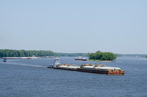 Barge traffic on the Mississippi River at Burlington, Iowa, USA. Tank barges in foreground haul ammonia, dry freight barges in background typically haul products like grain or cement.