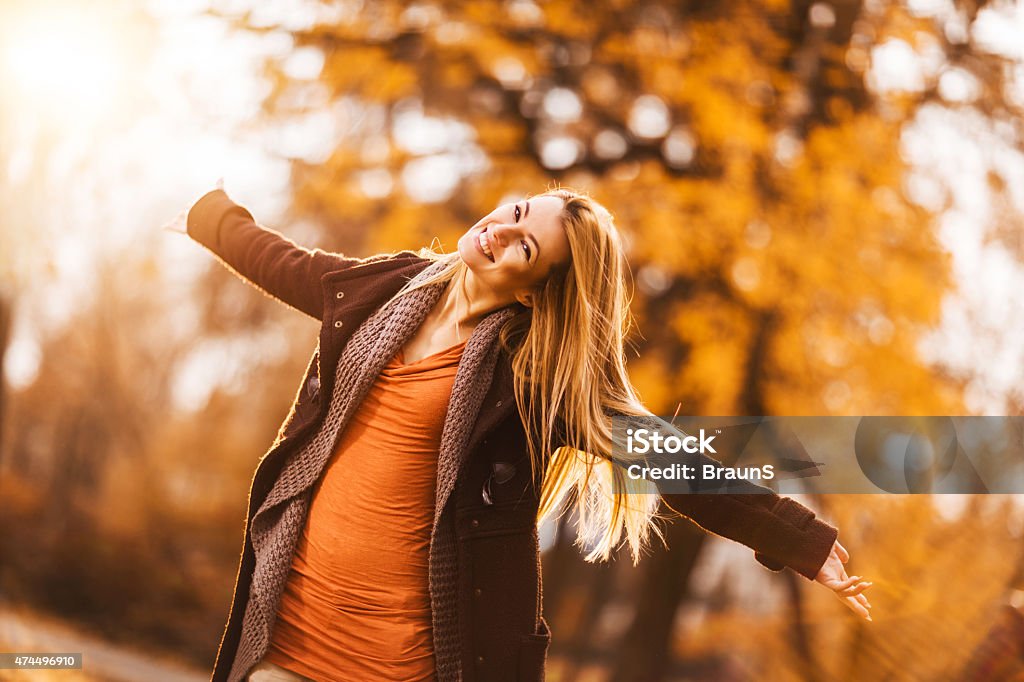 Carefree woman having fun in autumn day outdoors. Young happy woman standing in nature with her arms outstretched and looking at the camera. 2015 Stock Photo