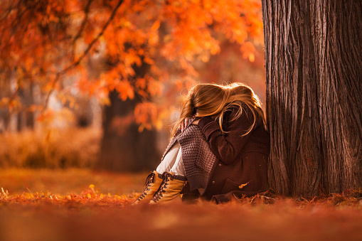 Depressed woman sitting in nature during autumn day and hiding her face.