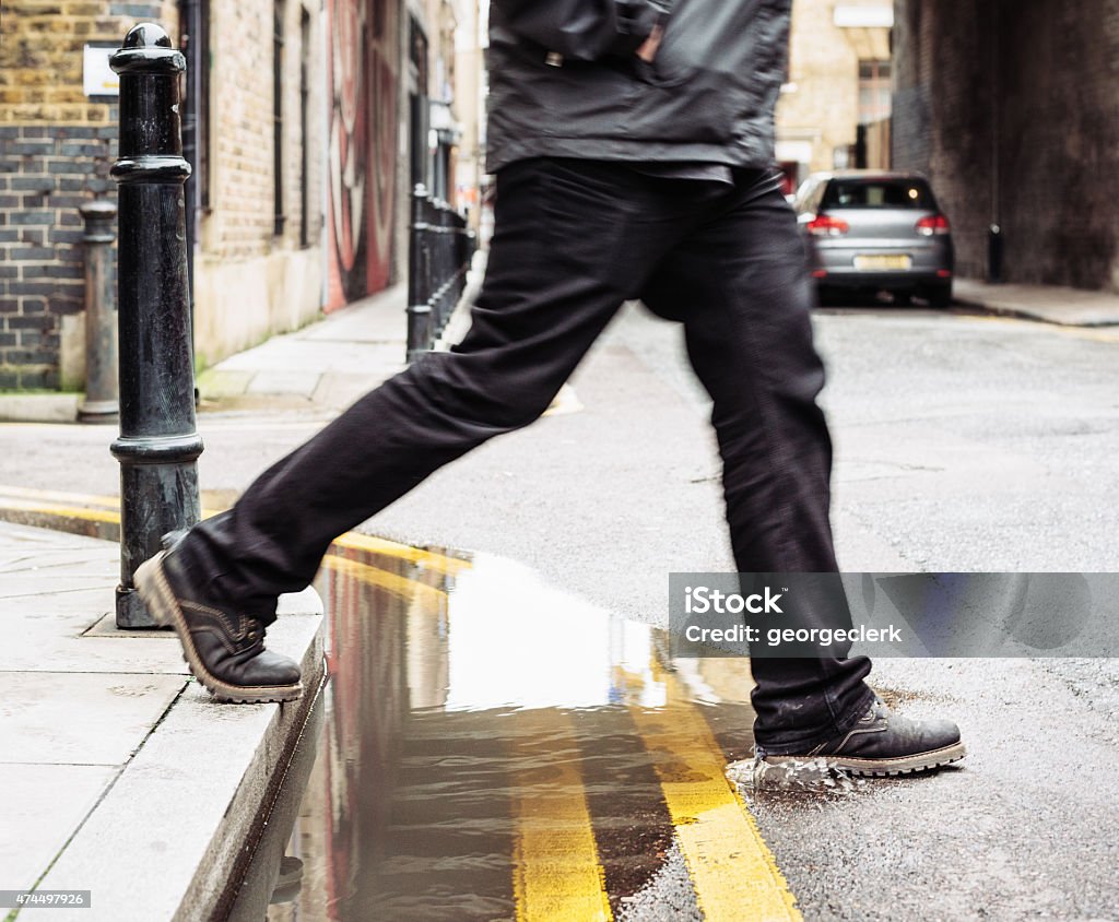 Stepping over a puddle A man stepping over a puddle between the pavement and street. Curb Stock Photo