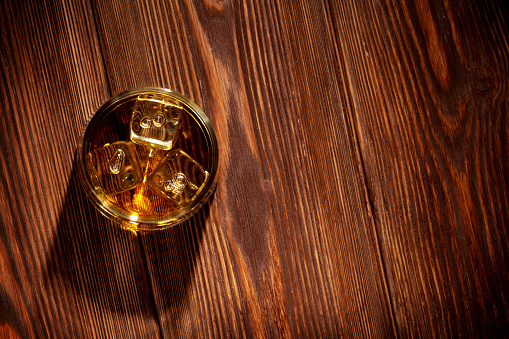 Glass of whiskey with ice on wooden table background. Top view with copy space