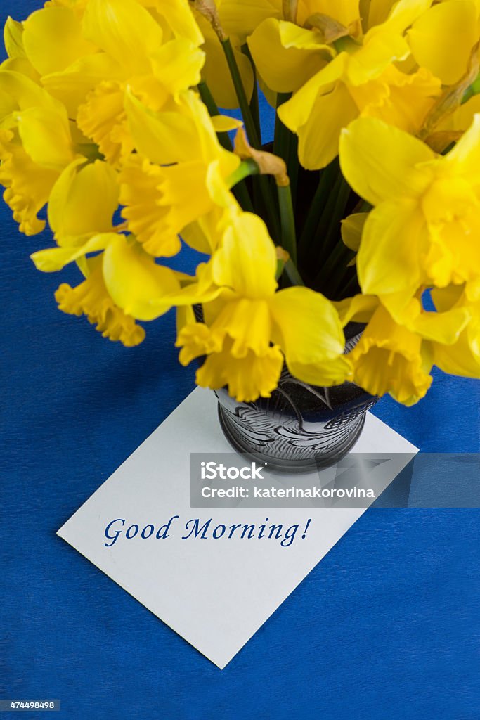 Bucket of narcissus flowers in vase, envelope on blue background Bucket of narcissus flowers in the black vase and an envelope on blue background with text 2015 Stock Photo