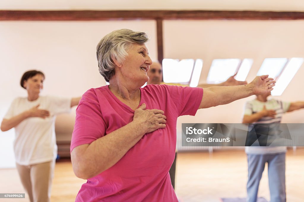 Group of smiling old people doing stretching exercises. Group of senior men and women exercising together in a health club. Focus is on foreground. Arms Outstretched Stock Photo