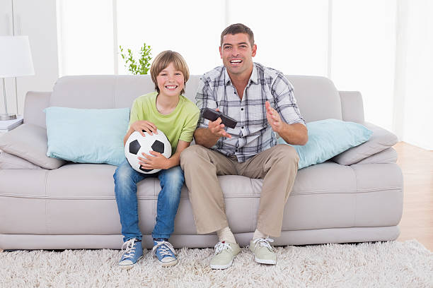 istock Happy boy watching soccer match with father on sofa 474501882