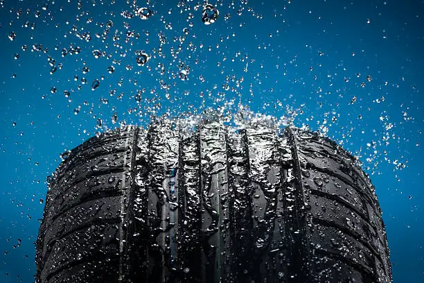 Photo of Water splashing on a new tire against blue background