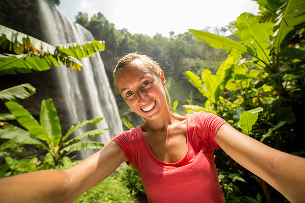 istock Girl in rain forest taking selfie with waterfall 474505034
