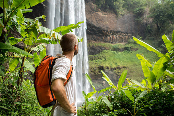 istock Man hiking in jungle looks at waterfall 474505104