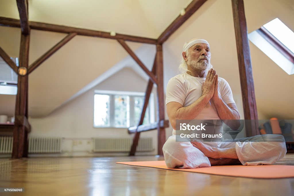 Below view of old man exercising Yoga in Lotus position. Low angle view of a senior man sitting in Lotus position at health club and meditating. 2015 Stock Photo