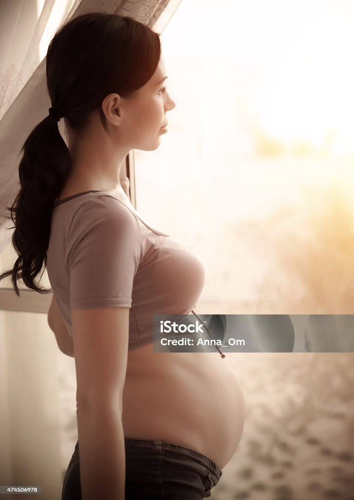 Sad pregnant woman Side view of sad pregnant woman looking at window, expecting female at home, new life concept 2015 Stock Photo