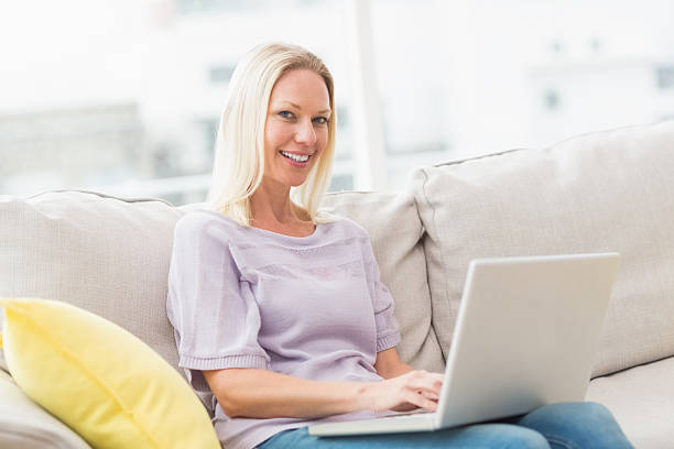 istock Smiling woman on sofa using laptop in living room 474510052