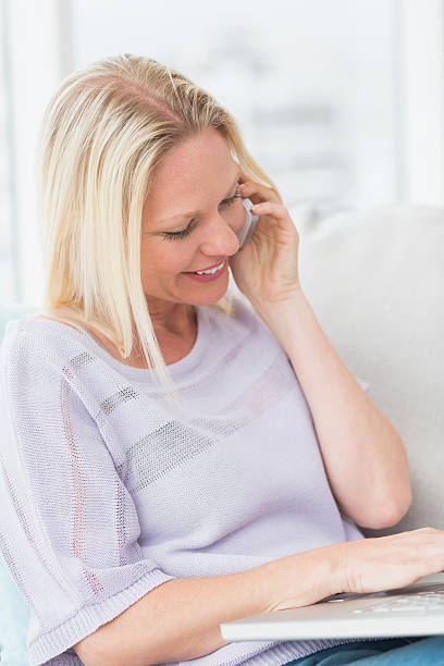 istock Woman talking on mobile phone while using laptop at home 474511388