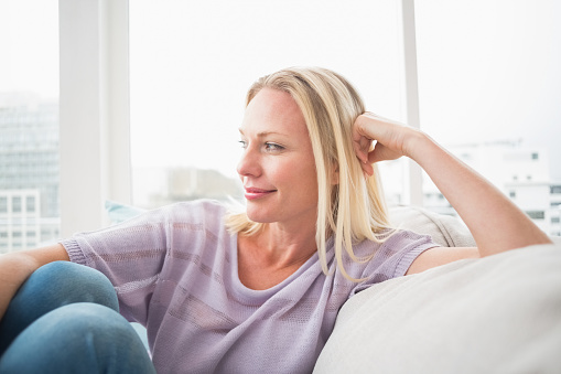 Thoughtful woman sitting on sofa in living room