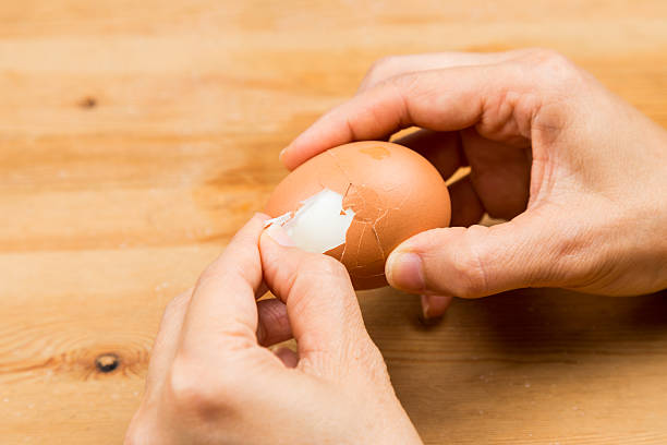 istock Fingers peeling hard boiled egg on wooden table 474512126