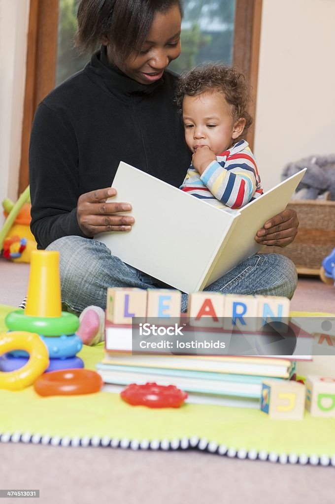 Portrait Of Carer Reading Book To Baby A portrait of an African American Carer reading a book to a baby. Baby - Human Age Stock Photo