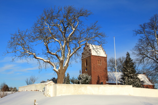 Medieval parish church on Zealand, Denmark with a surrounding wall and trees in snow covered winter landscape in December at Christmas time.