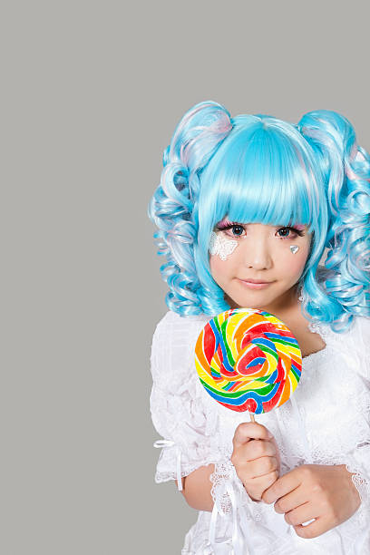 Portrait of cute young woman dressed as a doll holding lollipop over gray background