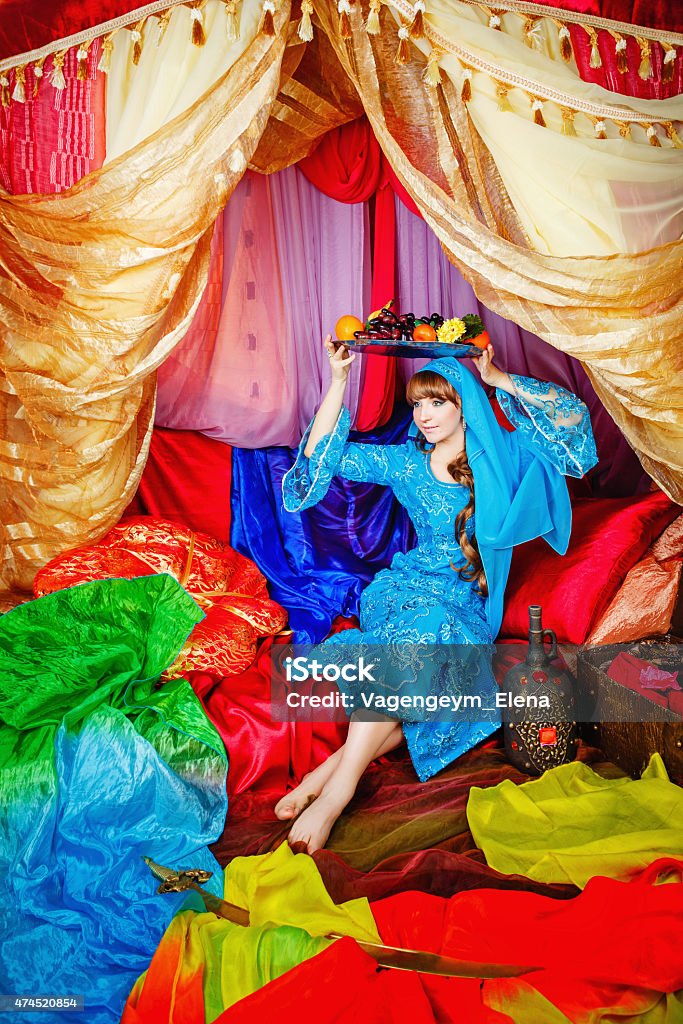 Asian Beauty holding platter with fruits Young Asian beauty sitting in a tent and holding on her head a dish with fruits. The concept of the Arab harem. 2015 Stock Photo