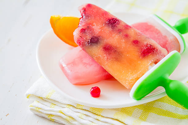 istock Fruit ice pops on white plate, orange slices, plaid napkin 474522764