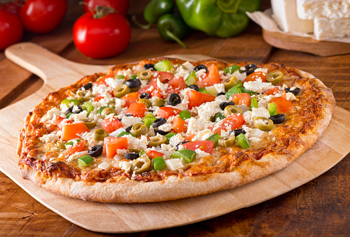 A delicious freshly baked greek pizza with feta cheese, olives, tomato, and green pepper.