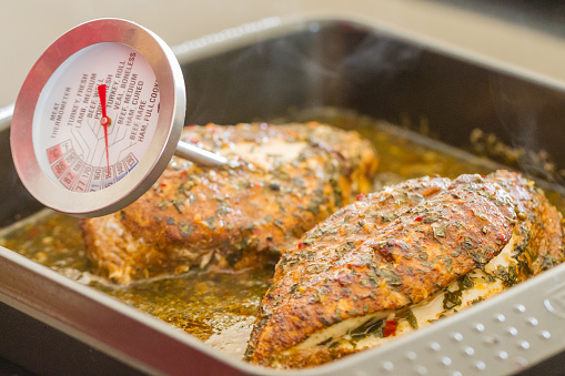 The temperature being measured of two seasoned chicken breasts in a baking tray.