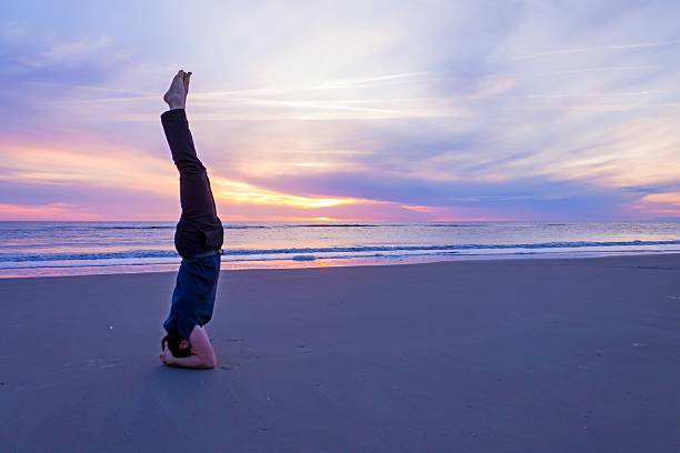 close to the origin A man carries out a handstand on a beach during sunset. shirshasana stock pictures, royalty-free photos & images