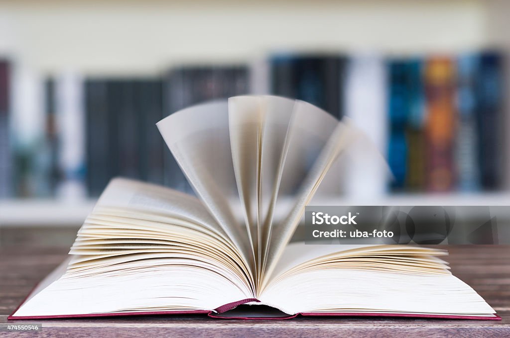 Opened book in front of bookcase Opened book in front of bookcase with flying pages and motion blur with selective focus. 2015 Stock Photo