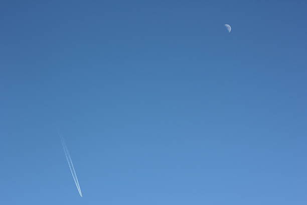 istock Moon and Aircraft, white condensation trail, clear blue sky 474559123