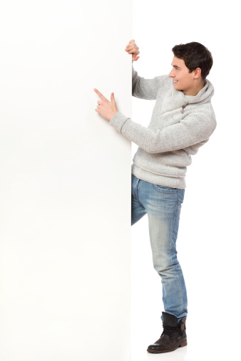 Handsome man in jeans and gray sweater pointing at a banner. Full length studio shot isolated on white.